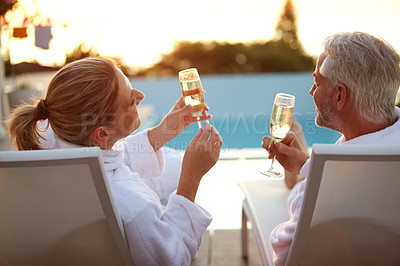 Buy stock photo Rearview shot of a mature couple drinking champagne while relaxing in deck chairs at sunset