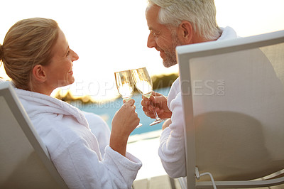 Buy stock photo Rearview shot of a mature couple drinking champagne while relaxing in deck chairs at sunset