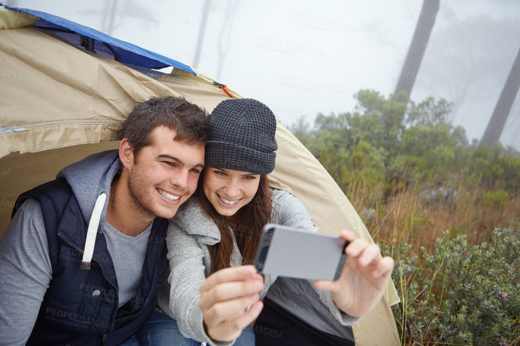 Buy stock photo Shot of a young couple taking a photo of themselves while sitting inside a tent