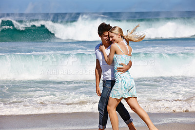 Buy stock photo Shot of a happy young couple enjoying a romantic walk along the beach