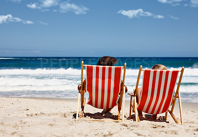 Buy stock photo Rearview shot of a couple reclining on their deck chairs at the water's edge