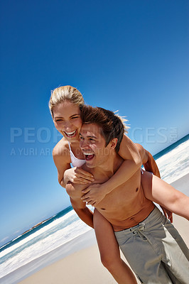 Buy stock photo Shot of a young man giving his girflfriend a piggyback ride at the beach