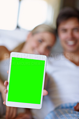 Buy stock photo Closeup shot of a happy couple lying in bed and holding up a digital tablet with a chroma key screen