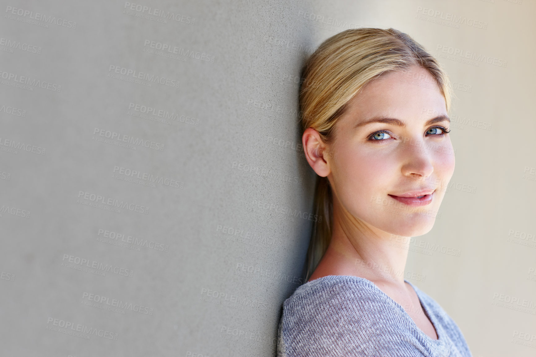 Buy stock photo Portrait of a happy young woman leaning against a gray wall