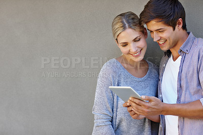 Buy stock photo Shot of a happy young couple using a digital tablet together against a gray background