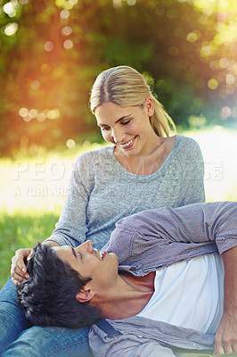 Buy stock photo Shot of a happy young couple lying on the grass and sharing an affectionate moment together
