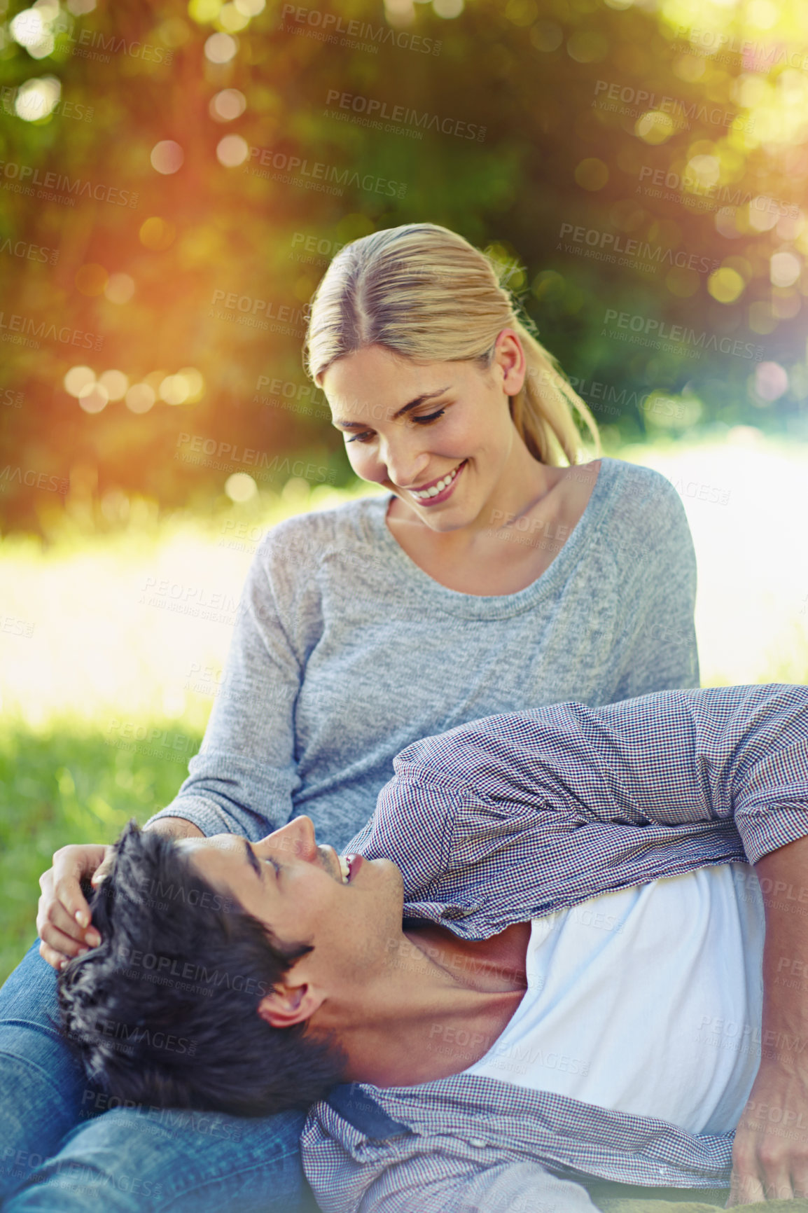 Buy stock photo Shot of a happy young couple lying on the grass and sharing an affectionate moment together