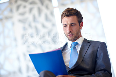 Buy stock photo Shot of a handsome young businessman reading a document in the office