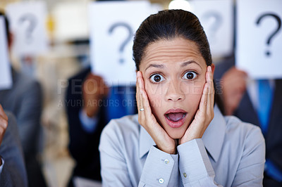 Buy stock photo Shot of a group of businesspeople holding up signs with question marks on them during a work presentation while their colleague looks surprised