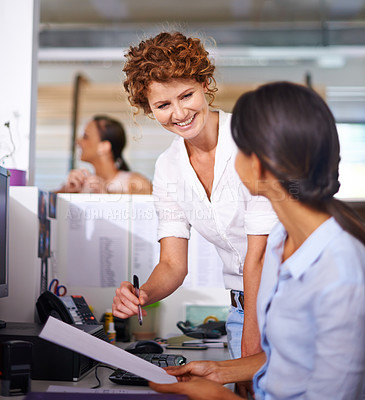 Buy stock photo Shot of a young woman talking to her colleague at her desk