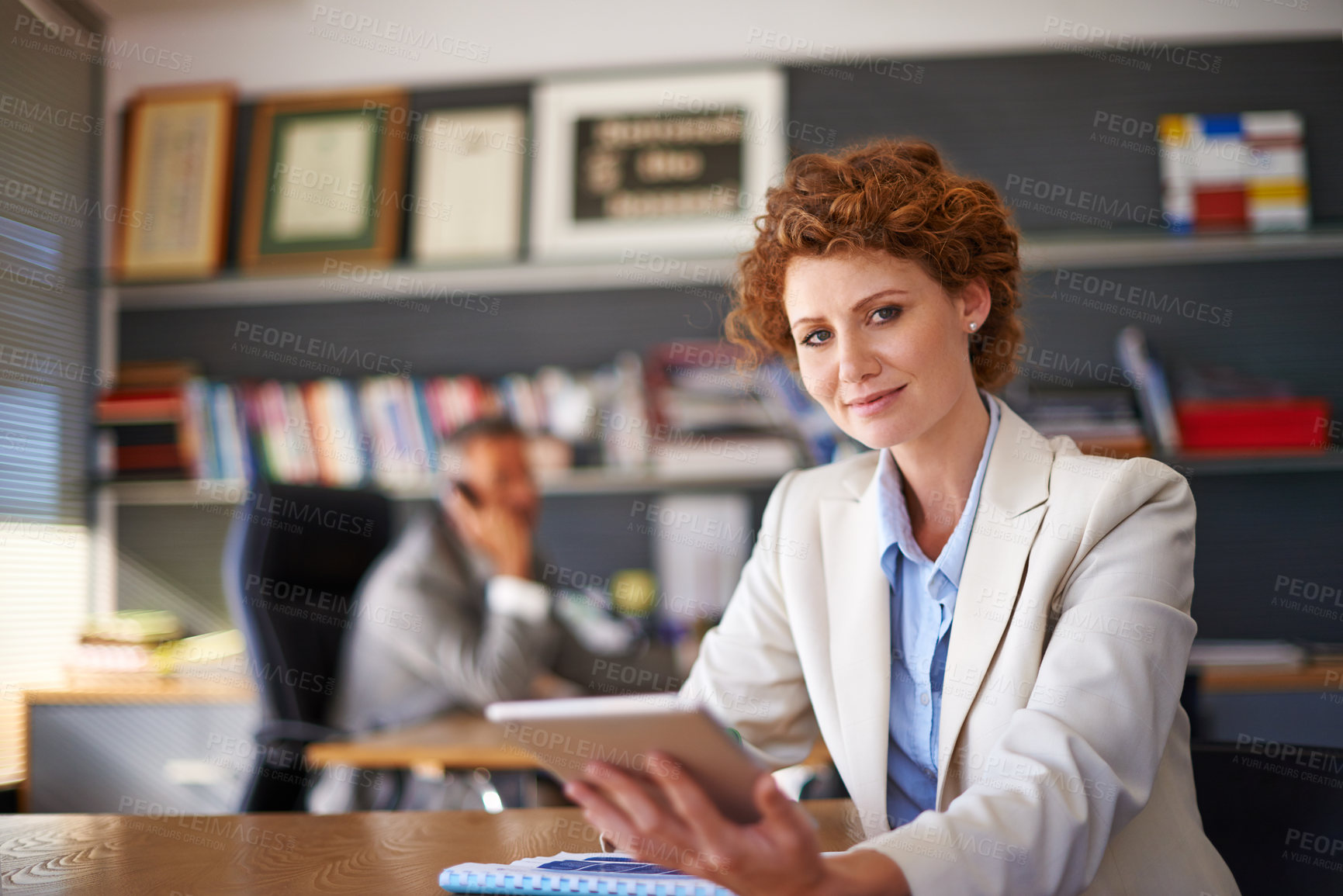 Buy stock photo Shot of a young female assistant using a tablet with her boss working in the background