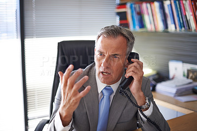 Buy stock photo Shot of a mature businessman looking angry while talking on the phone in his office