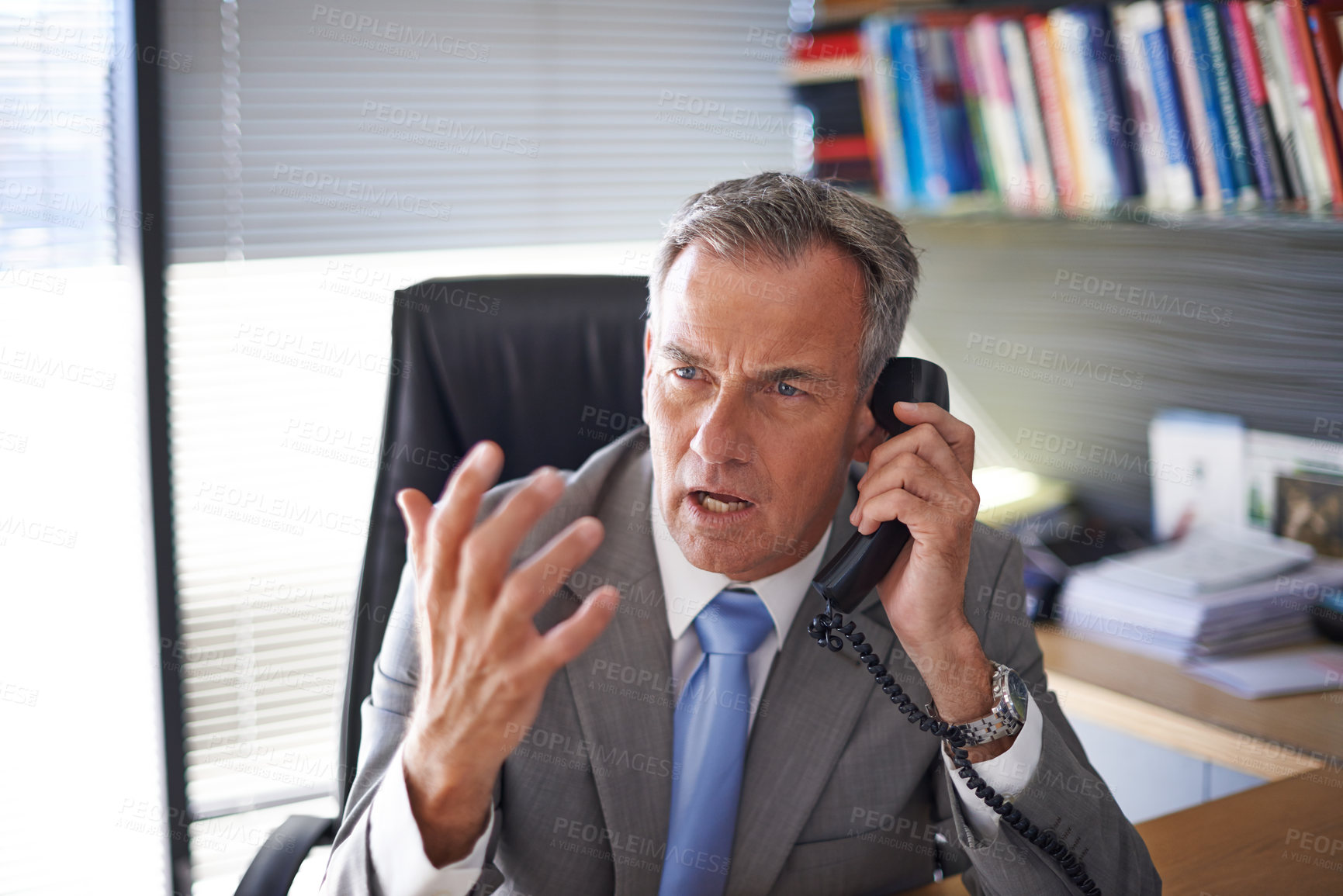 Buy stock photo Shot of a mature businessman looking angry while talking on the phone in his office