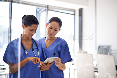 Buy stock photo Shot of two female nurses using a tablet to review medical records