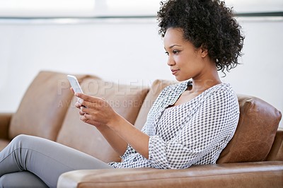 Buy stock photo Shot of an attractive woman using her smartphone while sitting on the sofa at home