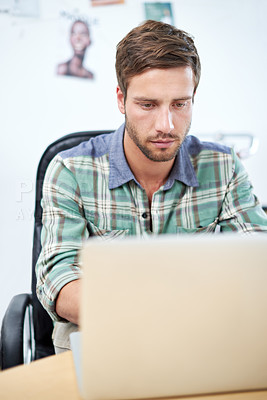 Buy stock photo Shot of a casually-dressed young man using a digital tablet at his desk. The commercial designs displayed  represent a simulation of a real product and have been changed or altered enough by our team of retouching and design specialists so that they don't have copyright infringements