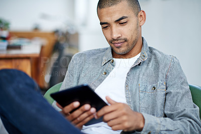Buy stock photo Shot of a handsome young office worker using a digital tablet while sitting in an office