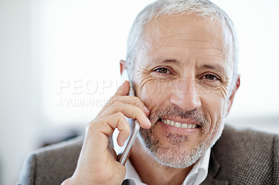Buy stock photo Portrait of a mature businessman talking on a cellphone while sitting at a table in an office