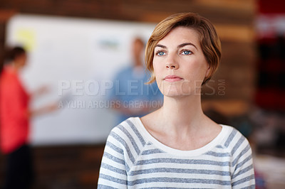 Buy stock photo A young female designer looking thoughtful while her colleagues work in the background
