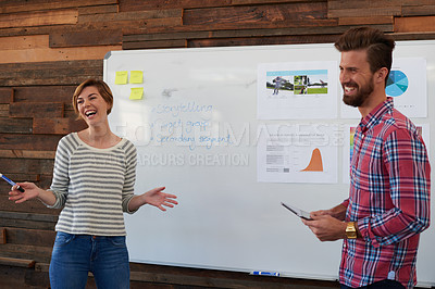 Buy stock photo Shot of two young designers brainstorming at a whiteboard