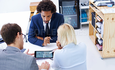 Buy stock photo Shot of a businessman viewing information on a digital tablet with two colleagues