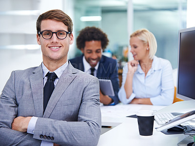 Buy stock photo Portrait of a smiling businessman sitting at his desk with staff in the background