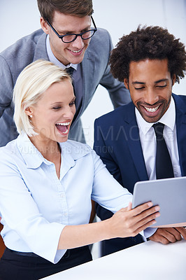 Buy stock photo Shot of three smiling colleagues looking at a digital tablet together