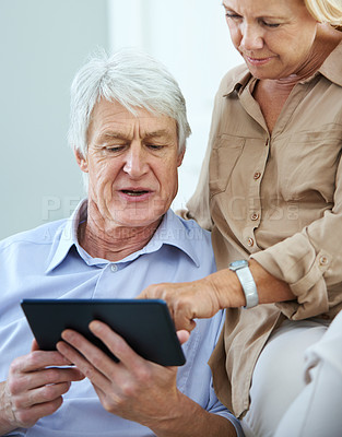 Buy stock photo Shot of a happy elderly couple using a digital tablet together at home