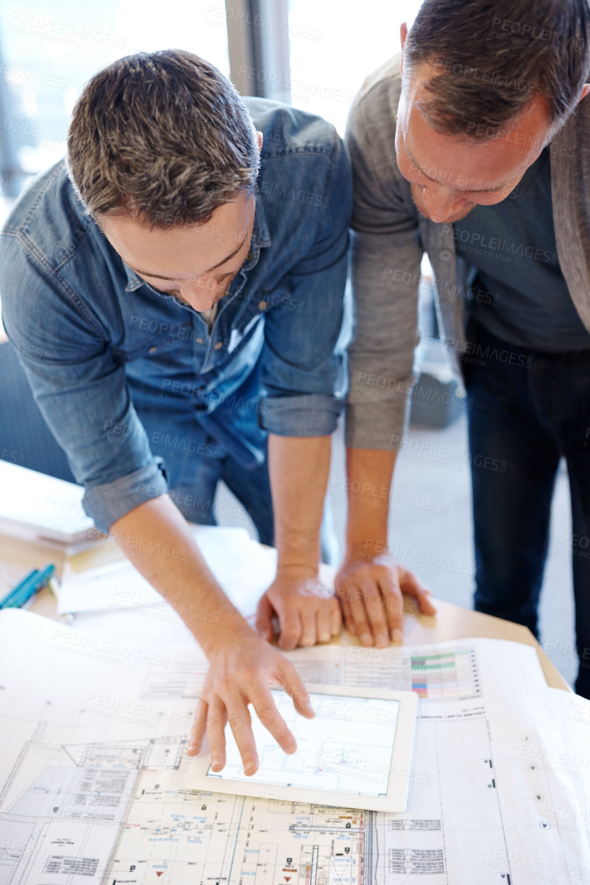 Buy stock photo Shot of two architects working together on a blueprint with the help of a digital tablet
