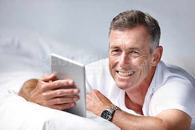 Buy stock photo Shot of a mature man using a digital tablet while lying on his bed