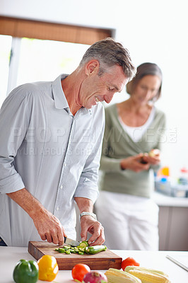 Buy stock photo Shot of a mature man chopping vegetables at a kitchen counter with his wife in the background