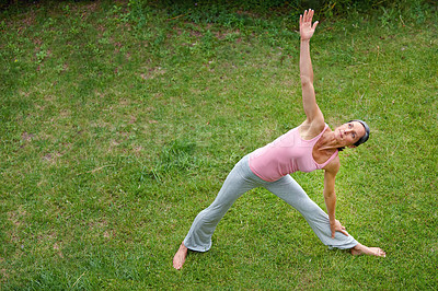 Buy stock photo Shot of a mature woman doing the extended triangle yoga pose outdoors