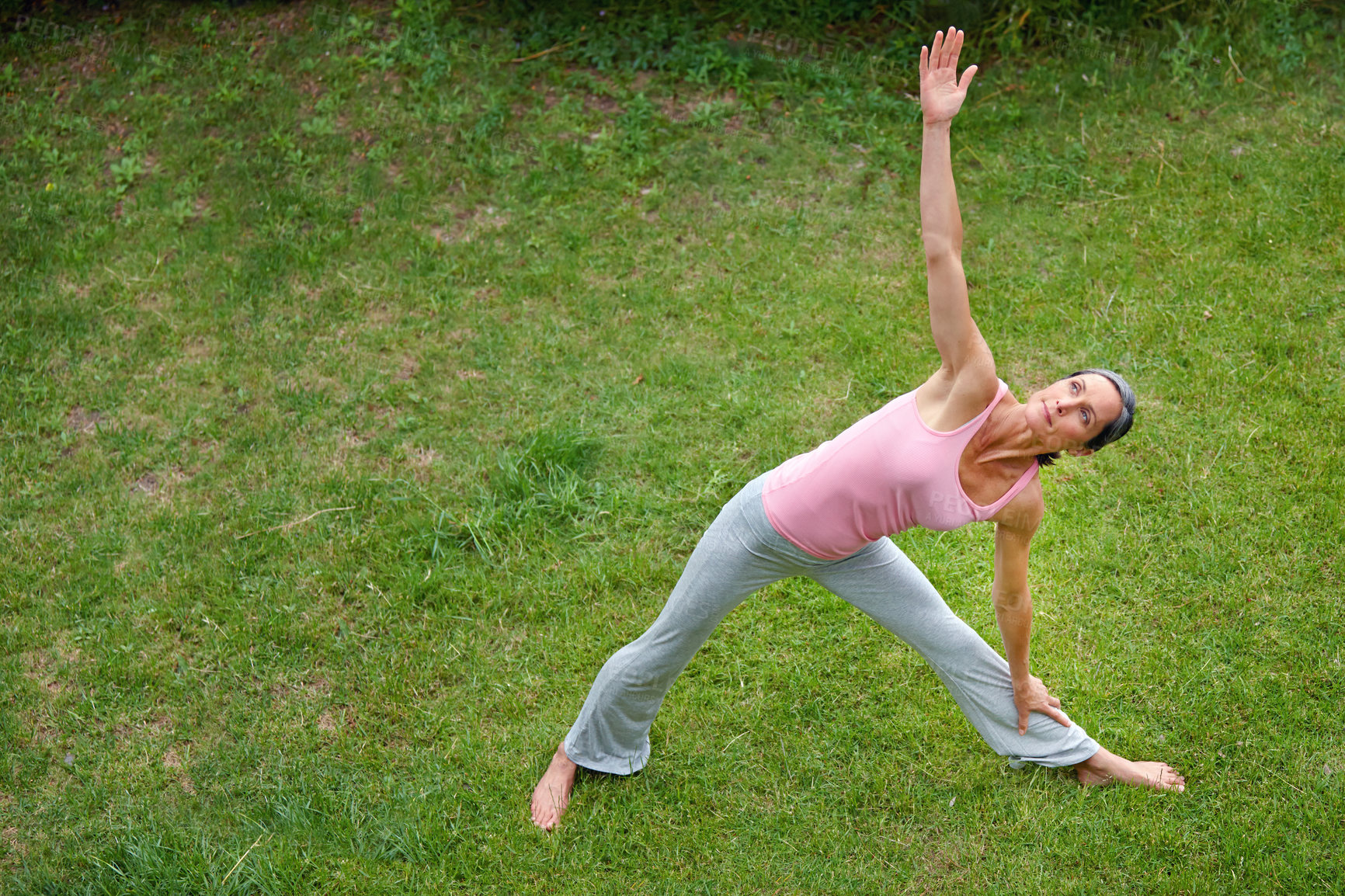 Buy stock photo Shot of a mature woman doing the extended triangle yoga pose outdoors