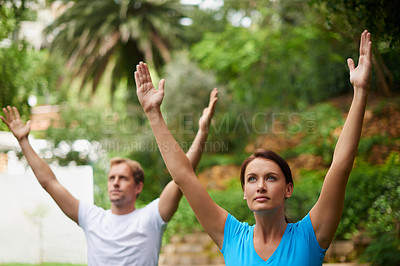 Buy stock photo Shot of a man and woman reaching upwards in an outdoor yoga class