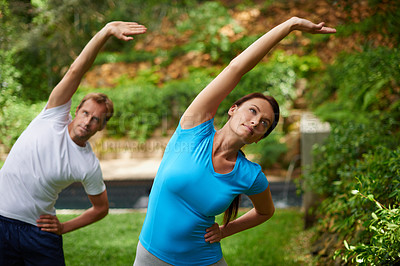 Buy stock photo Shot of a man and woman performing a side stretch in an outdoor yoga class
