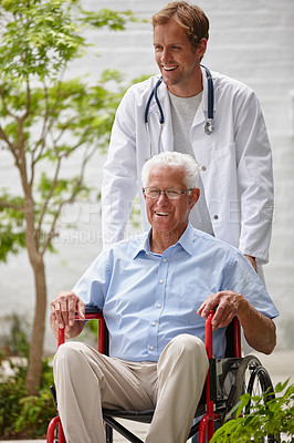 Buy stock photo Shot of a male doctor pushing his senior patient in a wheelchair outside