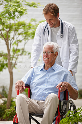 Buy stock photo Shot of a male doctor pushing his senior patient in a wheelchair outside