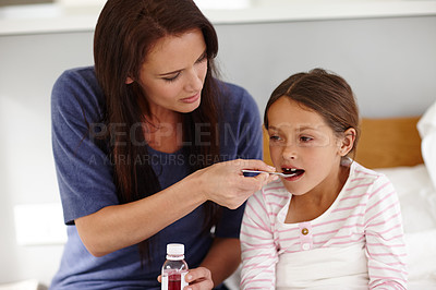 Buy stock photo Shot of a caring mother giving her sick little girl a spoonful of medicine 