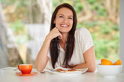 Buy stock photo Shot of a woman sitting in a kitchen eating breakfast