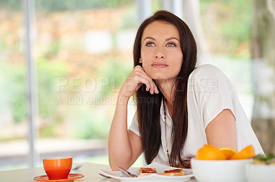 Buy stock photo Shot of a woman sitting in a kitchen eating breakfast