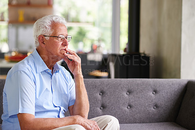Buy stock photo Shot of a thoughtful looking senior man sitting on his sofa