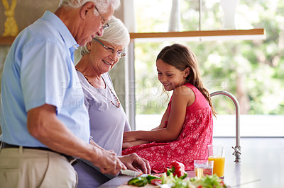 Buy stock photo Shot of a little girl helping her grandparents make lunch