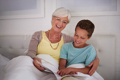 Buy stock photo A grandmother reading a book to her grandson in bed