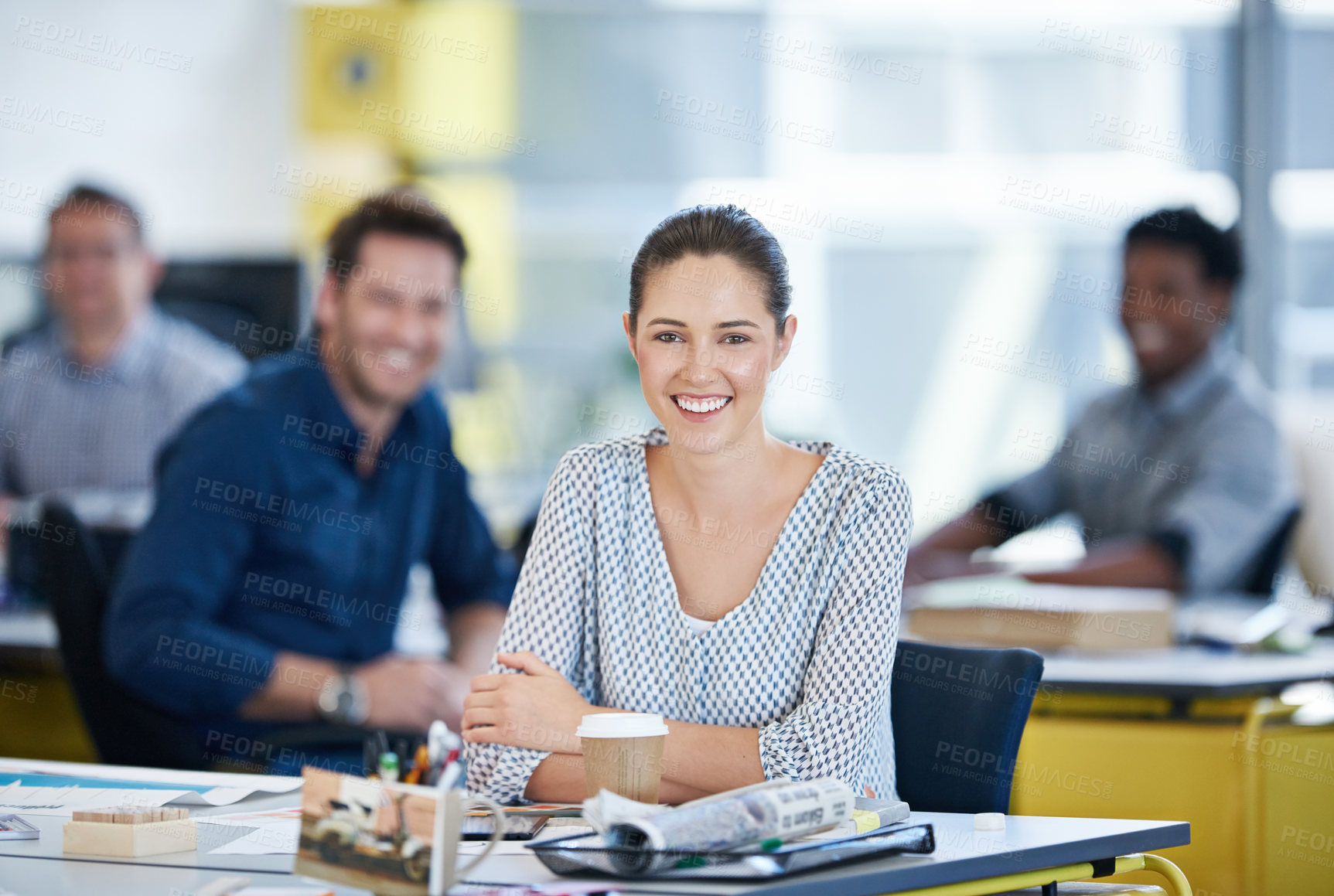 Buy stock photo Portrait of a young office worker at her desk with colleagues in the background