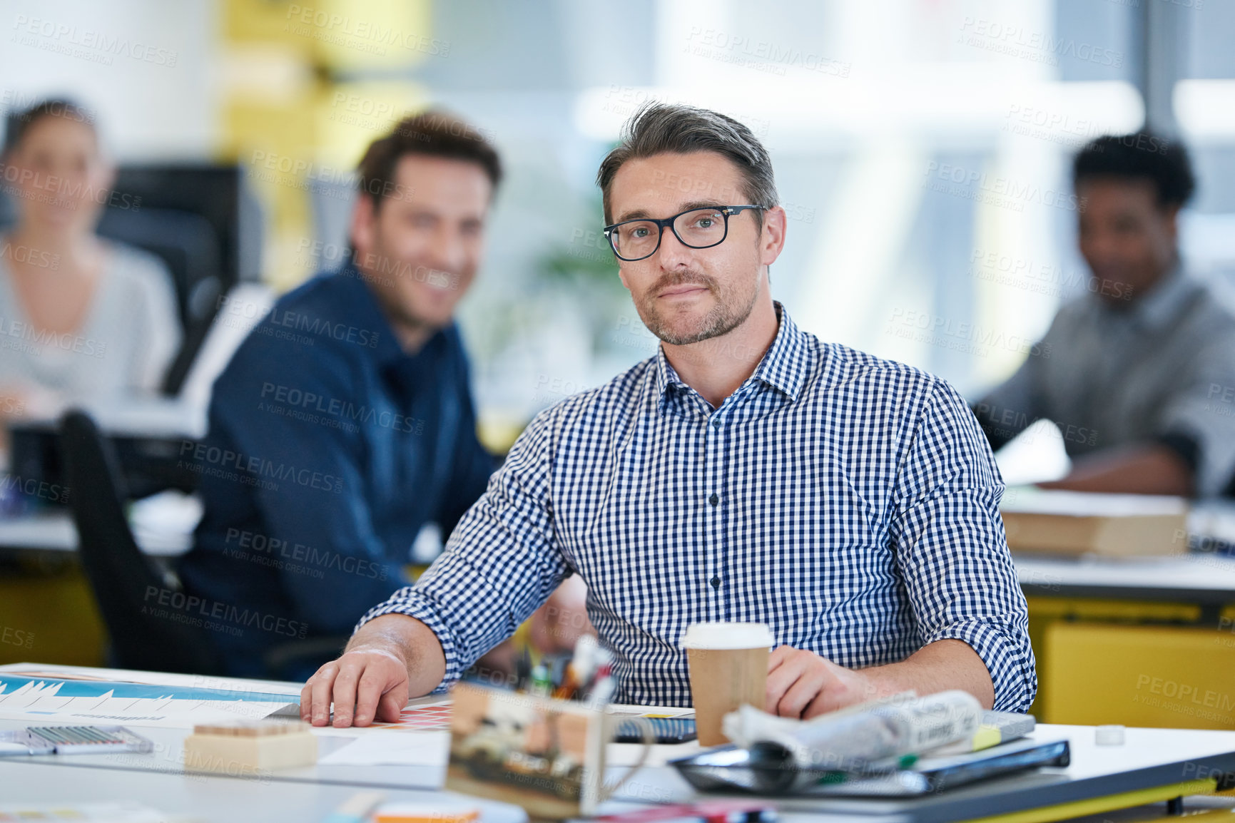 Buy stock photo Portrait of an office worker sitting at his desk with colleagues in the background