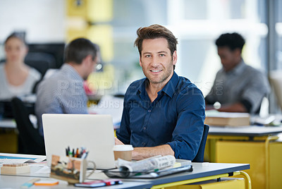 Buy stock photo Portrait of an office worker sitting at his desk working on a laptop with colleagues in the background