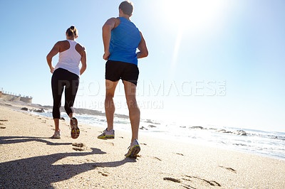 Buy stock photo Rearview shot of a young couple jogging together by the beach