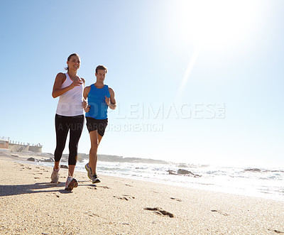 Buy stock photo Shot of a young couple jogging together by the beach