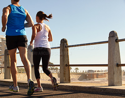 Buy stock photo Shot of a young couple jogging together on the promenade