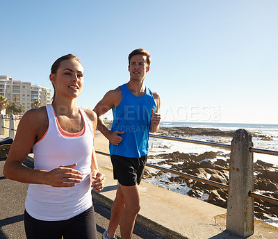 Buy stock photo Shot of a young couple jogging together on the promenade 